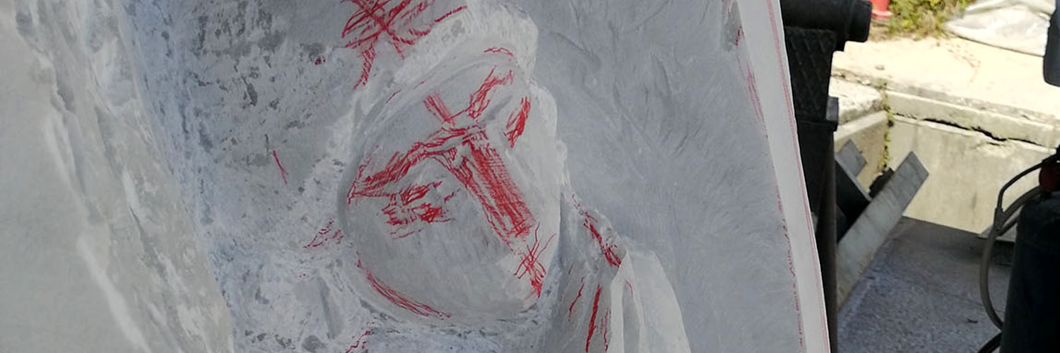 Bassorilievo di un angelo in lavorazione su una lastra di marmo, con i segni rossi del disegno